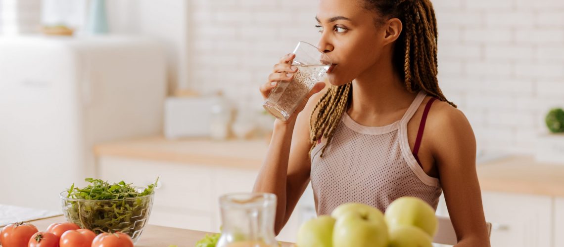 Slim and fit woman drinking water before having breakfast